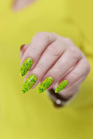 Female hand with long nails and neon green manicure with bottles of nail polish
