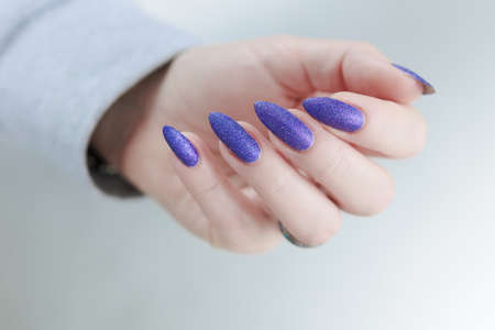 Female hand with long nails and purple plum manicure holds a bottle of nail polish