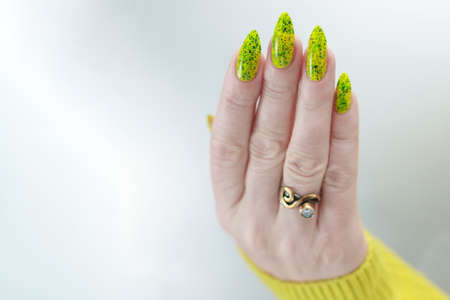 Female hand with long nails and neon green yellow manicure with bottles of nail polish