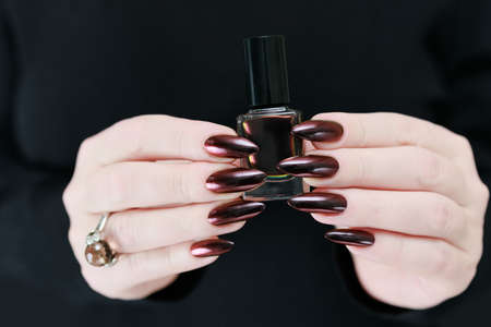 Female hand with long nails and dark red bordo manicure holds a bottle of nail polishの写真素材