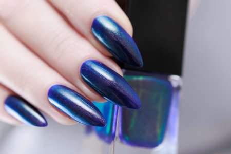 Woman's beautiful hand with long nails and turquoise green and blue manicure with bottles of nail...