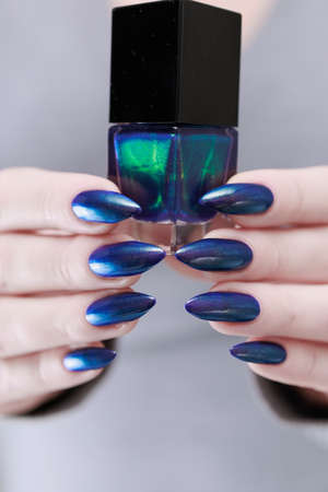 Woman's beautiful hand with long nails and turquoise green and blue manicure with bottles of nail...