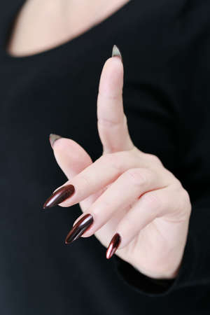 Female hand with long nails and dark red bordo manicure holds a bottle of nail polishの写真素材