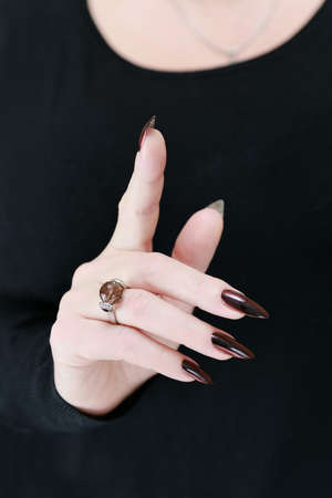Female hand with long nails and dark red bordo manicure holds a bottle of nail polishの写真素材