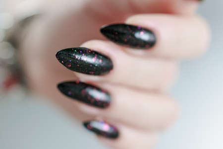 Female hands with long nails and total black manicure holding a bottle of nail polishの写真素材