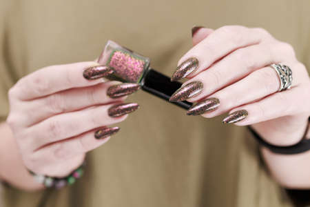 Female hand with long nails and a bottle of brown green nail polishの写真素材