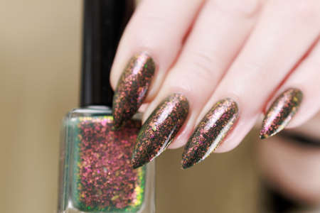 Female hand with long nails and a bottle of brown green nail polish