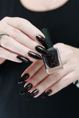 Female hands with long nails and total black manicure holding a bottle of nail polish