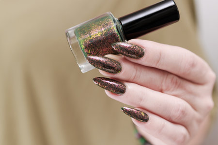 Female hand with long nails and a bottle of brown green nail polish