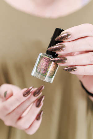 Female hand with long nails and a bottle of brown green nail polishの写真素材
