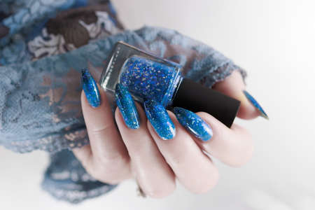 Woman's beautiful hand with long nails and bright blue manicure with bottles of nail polish