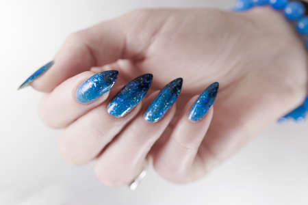 Woman's beautiful hand with long nails and bright blue manicure with bottles of nail polishの写真素材