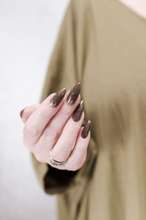 Female hand with long nails and a bottle of brown green nail polishの写真素材