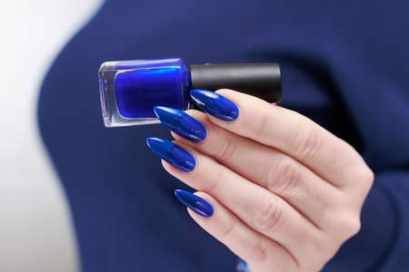 Woman's beautiful hand with long nails and bright blue manicure with bottles of nail polish