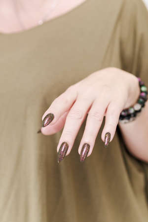 Female hand with long nails and a bottle of brown green nail polishの写真素材