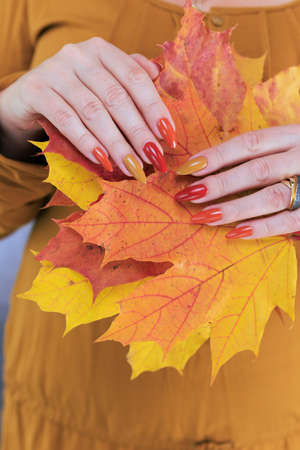 Female hand with long nails and a bottle of bright red orange yellow nail polish