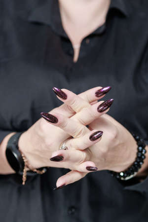 Female hand with long nails and dark purple burgundy manicure holds a bottle of nail polishの写真素材