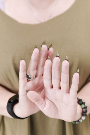 Female hand with long nails and a bottle of brown green nail polishの写真素材
