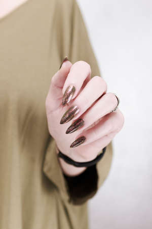 Female hand with long nails and a bottle of brown green nail polish