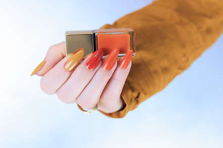 Female hand with long nails and a bottle of bright red orange yellow nail polish