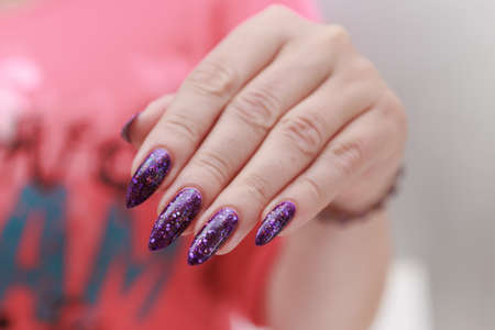 Female hand with long nails and purple plum manicure holds a bottle of nail polishの写真素材