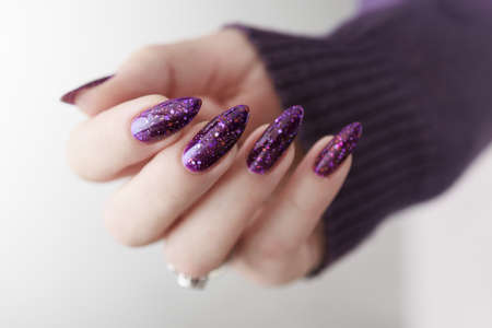 Female hand with long nails and purple plum manicure holds a bottle of nail polishの写真素材