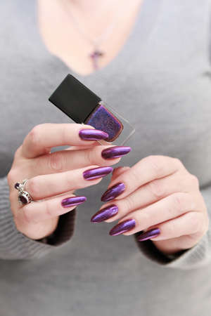 Female hand with long nails and purple plum manicure holds a bottle of nail polishの写真素材