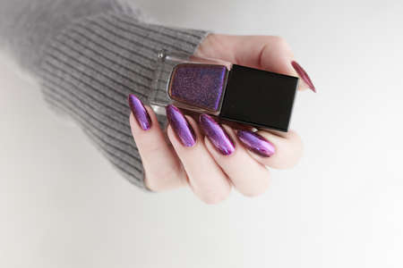 Female hand with long nails and purple plum manicure holds a bottle of nail polish