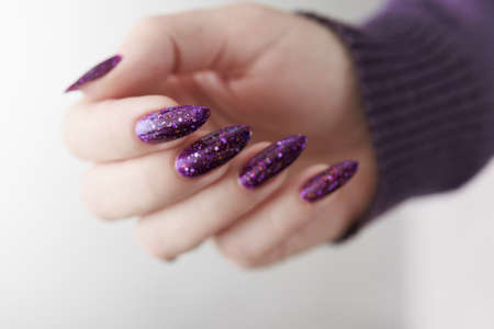 Female hand with long nails and purple plum manicure holds a bottle of nail polish