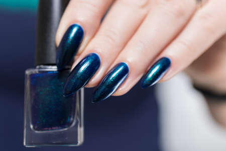 Woman's beautiful hand with long nails and turquoise green and blue manicure with bottles of nail polishの写真素材