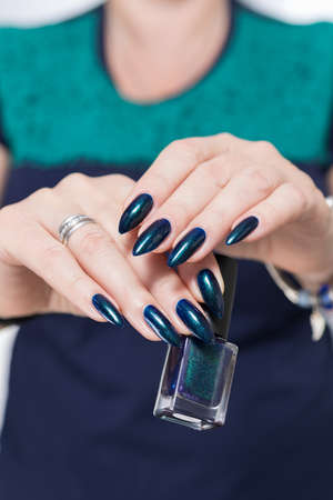 Woman's beautiful hand with long nails and turquoise green and blue manicure with bottles of nail polishの写真素材