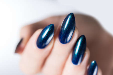 Woman's beautiful hand with long nails and turquoise green and blue manicure with bottles of nail polishの写真素材