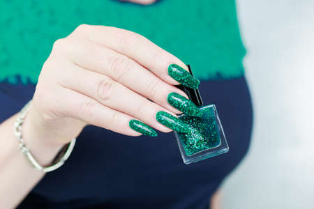 Female hand with long nails and neon green manicure with bottles of nail polish