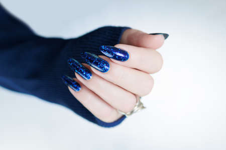 Woman's beautiful hand with long nails and bright blue manicure with bottles of nail polishの写真素材