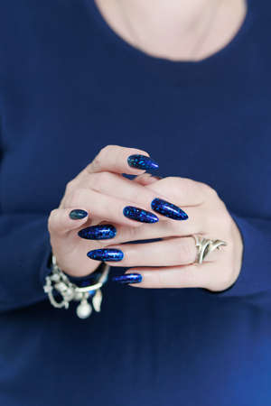 Woman's beautiful hand with long nails and bright blue manicure with bottles of nail polishの写真素材
