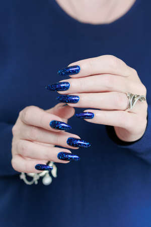 beautiful female hand with long nails and blue manicure with bottles of nail polishの写真素材