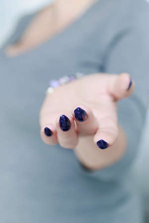 beautiful female hand with long nails and blue manicure with bottles of nail polishの写真素材