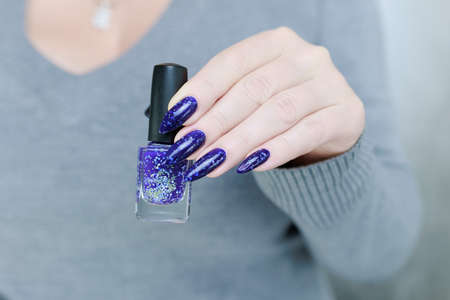 beautiful female hand with long nails and blue manicure with bottles of nail polish