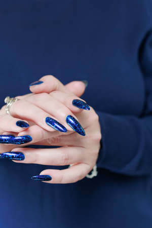 beautiful female hand with long nails and blue manicure with bottles of nail polishの写真素材