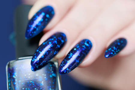 Woman's beautiful hand with long nails and bright blue manicure with bottles of nail polishの写真素材