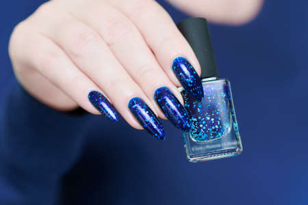 Woman's beautiful hand with long nails and bright blue manicure with bottles of nail polishの写真素材