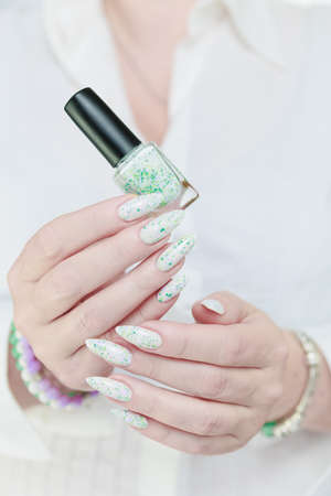 beautiful female hands with long nails light white manicure and a bottle of nail polish