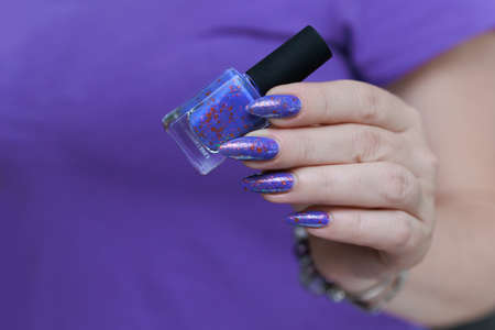 Female hand with long nails and a bottle of light lilac color nail polish
