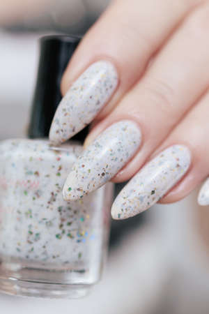 beautiful female hands with long nails light white manicure and a bottle of nail polish