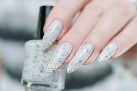 beautiful female hands with long nails light white manicure and a bottle of nail polishの写真素材