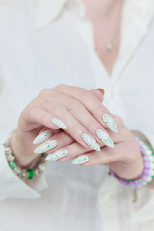 beautiful female hands with long nails light white manicure and a bottle of nail polishの写真素材