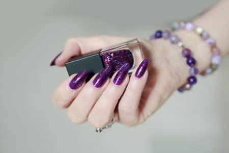 Female hand with long nails and purple plum manicure holds a bottle of nail polishの写真素材
