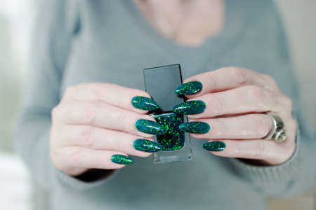 Female hands with long nails and green manicure with bottles of nail polish