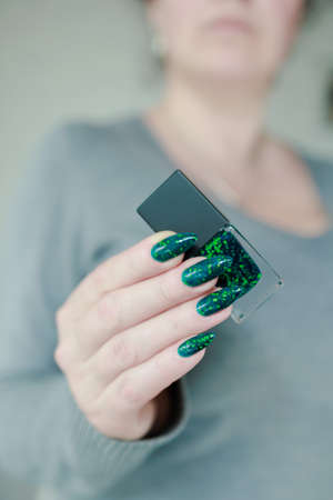 Female hands with long nails and green manicure with bottles of nail polish