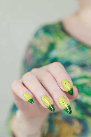 Woman's hand with long nails and bright yellow green thermo manicure with bottles of nail polishの写真素材